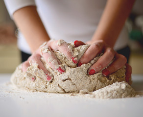 Woman's hands knead dough on a table