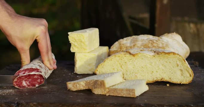 Chef cutting with a knife fine italian high quality salami in slices. original recipe and tradition. composition with bread and cheese 