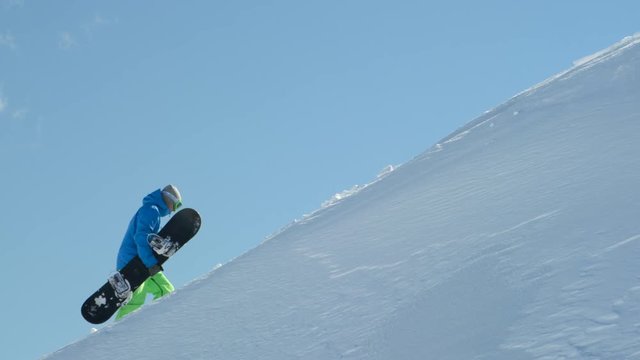 Extreme freeride snowboarder hiking towards mountaintop to ride powder snow