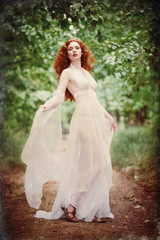 Obraz na płótnie Canvas Gorgeous redhead woman wearing white dress in a forest. Grunge texture effect