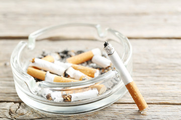 Cigarette butts with ash in ashtray on grey wooden table
