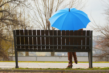 Lonely girl with blue umbrella siting on bench in  rainy day