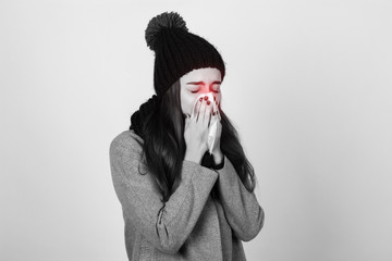 Portrait of a pretty woman with scarf and hat having flu. girl blowing nose standing over gray background black and white with red accent