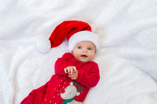 cheerful a baby girl with blue eyes in santa hat lying on a bed