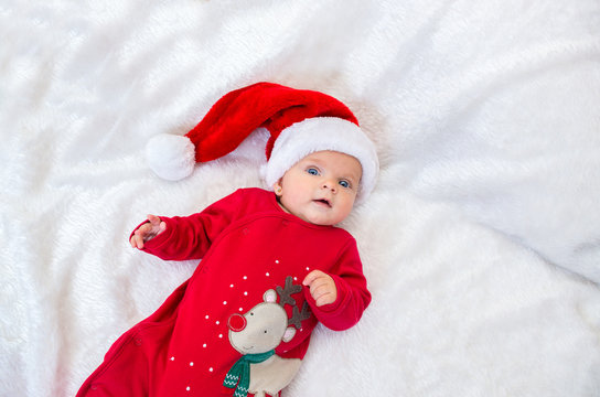 cheerful a baby girl with blue eyes in santa hat lying on a bed