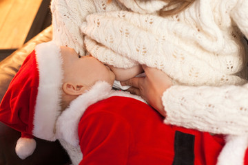 Newborn baby wearing as Santa Claus breast feeding. Selective focus on the kid s face. Homemade Christmas