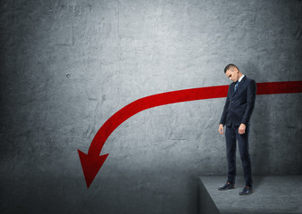 Upset businessman standing on the edge of abyss with red arrow going down