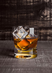 Glasss of whiskey with ice cubes on wood