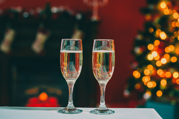 Beautiful two glasses of champagne standing on the table in the background of a blurred room with a decorated Christmas tree and fireplace. Soft focus. Shallow DOF