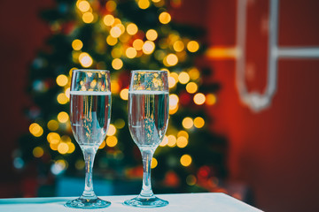 Beautiful two glasses of champagne standing on the table in the background of a blurred room with a decorated Christmas tree and fireplace. Soft focus. Shallow DOF
