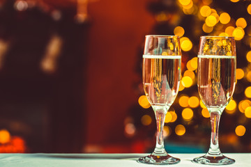 Beautiful two glasses of champagne standing on the table in the background of a blurred room with a decorated Christmas tree and fireplace. Soft focus. Shallow DOF