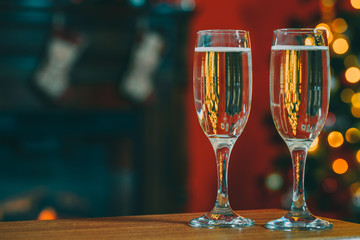 Beautiful two glasses of champagne standing on the table in the background of a blurred room with a decorated Christmas tree and fireplace. Soft focus. Shallow DOF