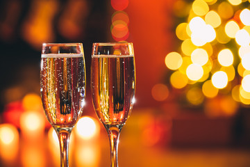 Beautiful two glasses of champagne standing on the table in the background of a blurred room with a decorated Christmas tree and fireplace. Soft focus. Shallow DOF