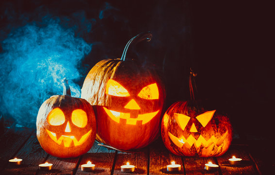 Three glowing pumpkins symbolizing the head of old Jack, with smoke on wooden background. Soft focus. shallow DOF