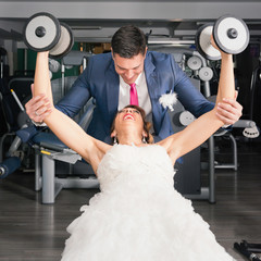 Bride and groom in the gym. Groom helping bride with weights