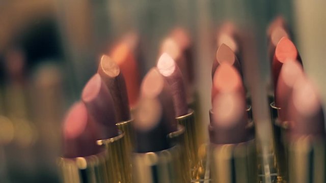 Lipstick variety of colors and shades in the shop window sparkle in the rays of light. Closeup. Shallow depth of field. Dolly shot