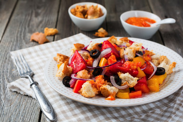 Salad with peppers, tomatoes, onions, olives and croutons with sousomna old wooden background. Selective focus.