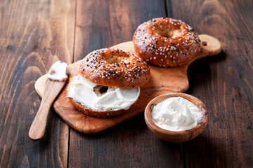 Whole grain bagels with cream cheese on wooden board, selective focus