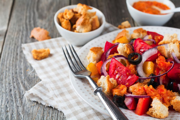 Salad with peppers, tomatoes, onions, olives and croutons with sousomna old wooden background. Selective focus.