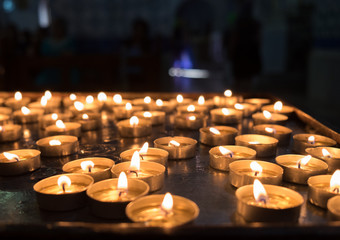 lit votive candles in church on black background - obrazy, fototapety, plakaty