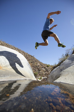 An adult man jumping from one rock to another over the top of the waterfall at Sierra de la Laguna.  Baja California, Mexico.