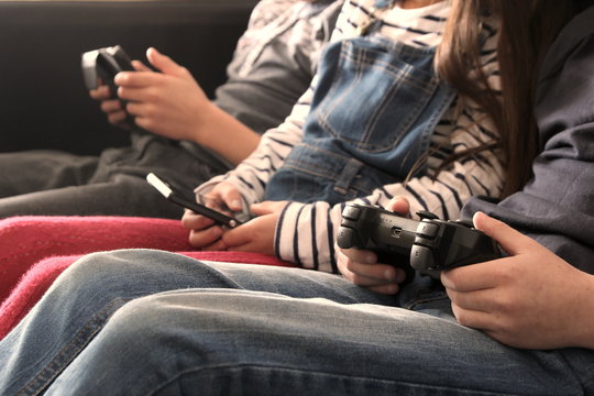 Three children playing with electronic devices - tablet, smartphone, games controller