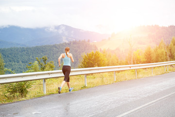Obraz premium Young athletic woman jogging on road in mountains