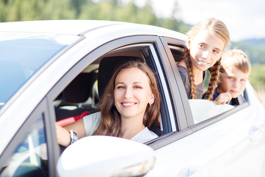 Happy Young Mom And Her Children Sitting In A Car