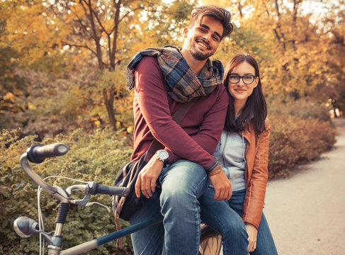Young couple riding bicycle outdoors at autumn.They sitting on bike and looking at camera.