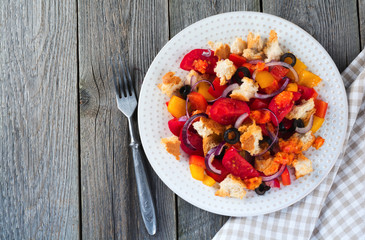 Salad with peppers, tomatoes, onions, olives and croutons with sauce old wooden background. Selective focus.