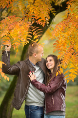 Young couple are enjoying their time together in a park on a beautiful Autumn day. They are hugging and looking to each other.