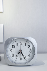 white square clock on white bed stand with white wallpaper background, morning time in minimal style decoration.