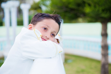 Young First Communion boy smiling and leaning on a white wooden