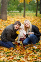 Happy parents with baby daughter among yellow leaves