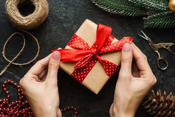 top view of female hands wrapping christmas gift decorated with red ribbon