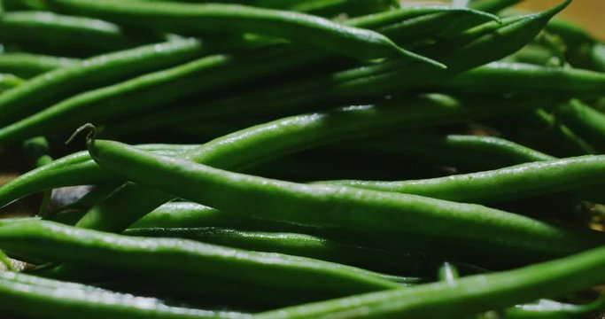 Super slow motion macro of falling green string beans on a wooden kitchen table in 4k
