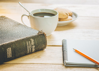 image of the old book with small note book, pencil and a cup of coffee on wooden background