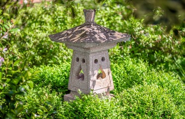 A Japanese stone lantern under a tree in the shade and surrounded by green leaves