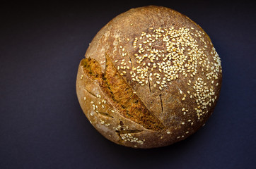 Fresh homemade rye bread sprinkled with sesame seeds on dark background