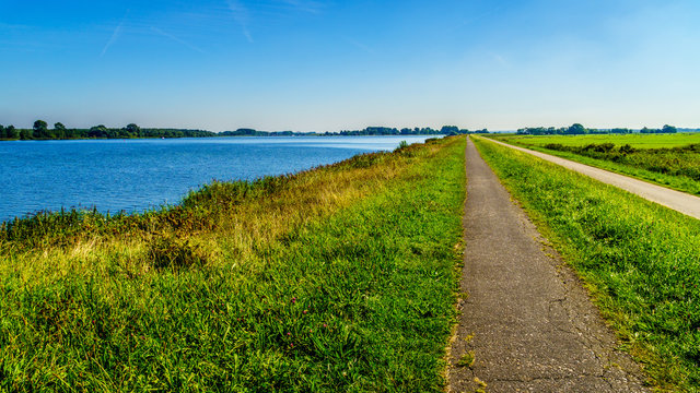 TStraight bicycle path over the dike along the the bird sanctuary of Veluwemeer surrounded by reed and meadows under blue sky near the town of Nijkerk in the Netherlands