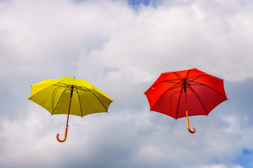 Yellow and red umbrella or parasols floating suspended in the air under cloudy sky