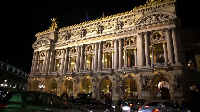 Cars driving past illuminated Academie Royale de Musique in Paris, traffic jam