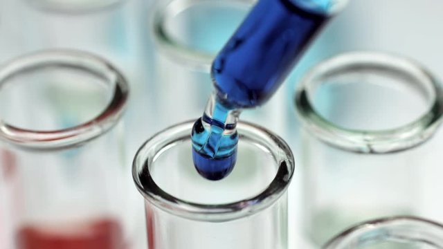 Macro shot of droppig three drops of blue liquid in test tube with glass dropper