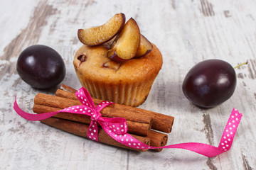 Fresh baked muffins with plums and cinnamon sticks on old wooden background, delicious dessert