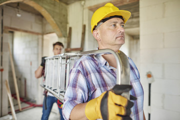 Side view of carrying ladder by two carpenters.