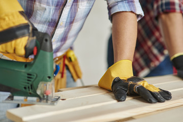 Carpenter is sawing wooden planks by electric saw