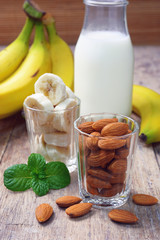 Almond nuts and sliced banana in glass with almond milk in bottle.