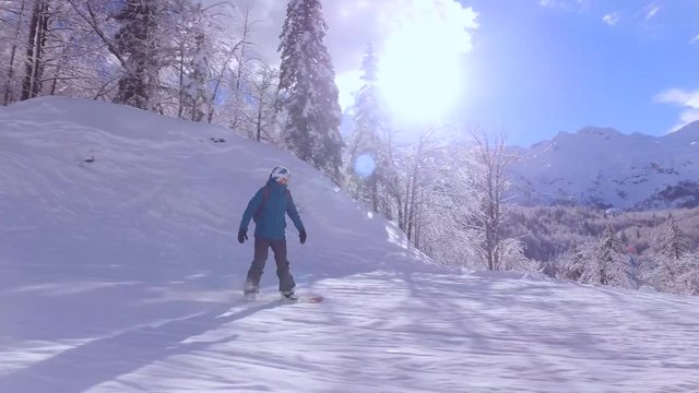 Snowboarder girl snowboarding down the ski slope in sunny mountain ski resort