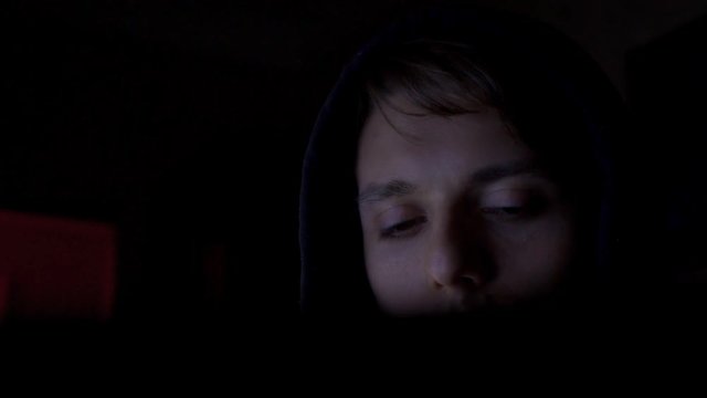 Hacker in hood cracking code using computers in dark room close up
