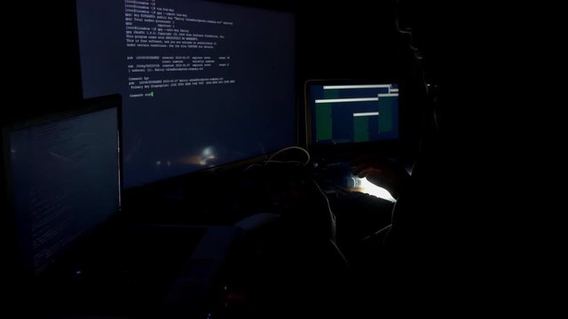 Hacker in hood cracking code using computers in dark room